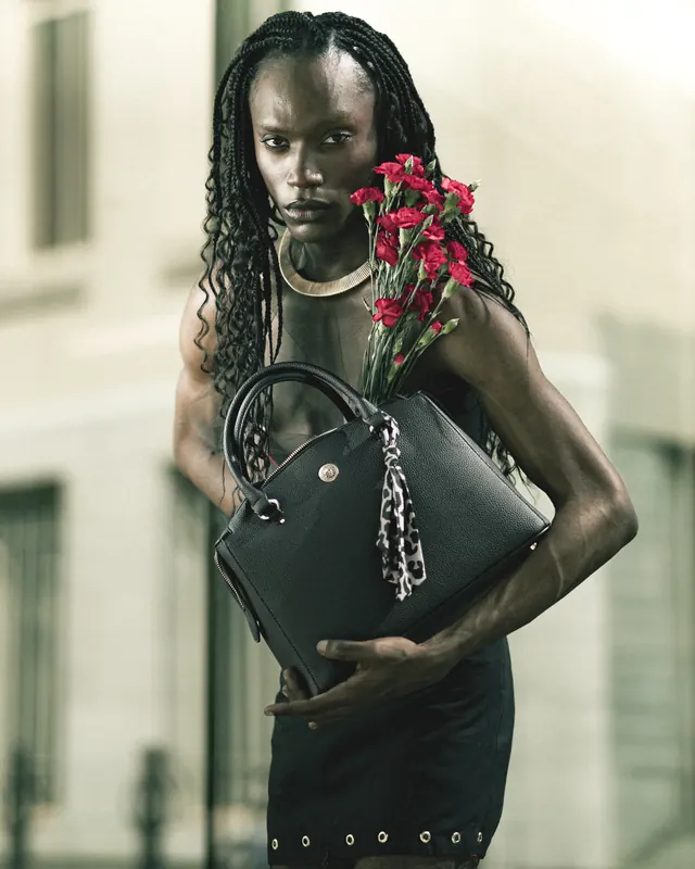 Model with long braids and a gold collar holding a black handbag and red carnations